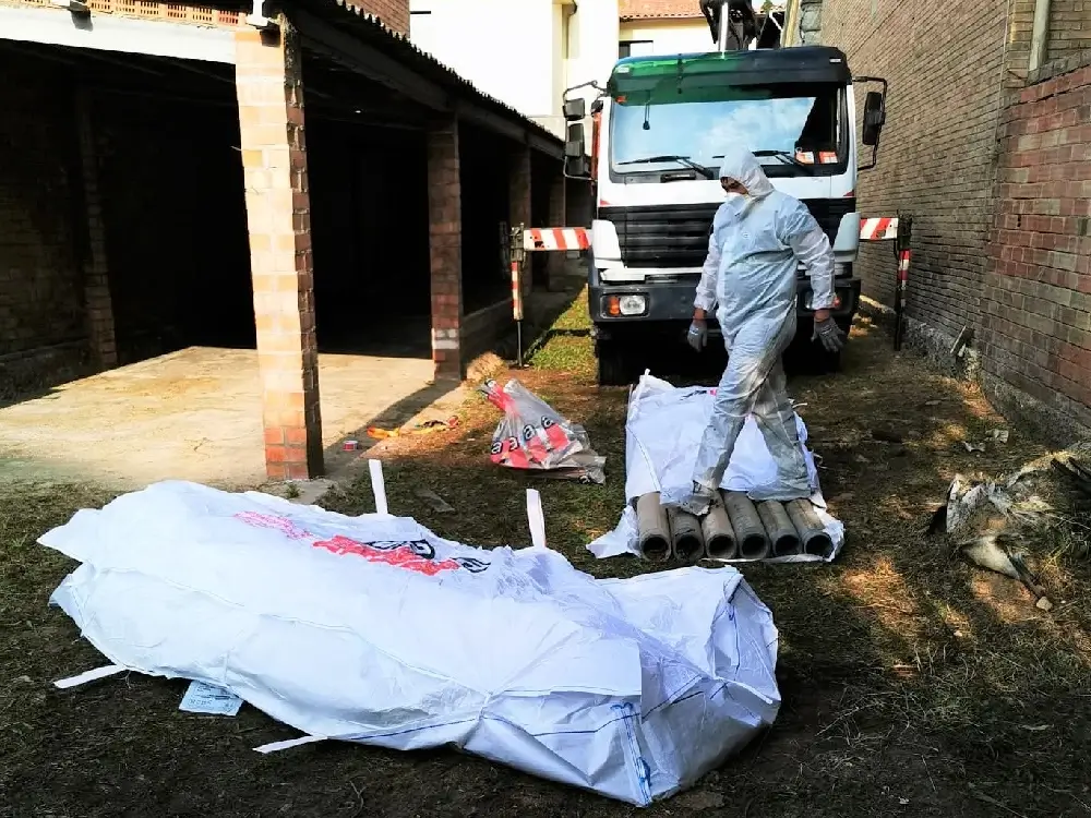 Trabajador de retirada de amianto con su ropa EPI envolviendo residuos en una bolsa especial para residuos de amianto con un camión de la empresa de fondo