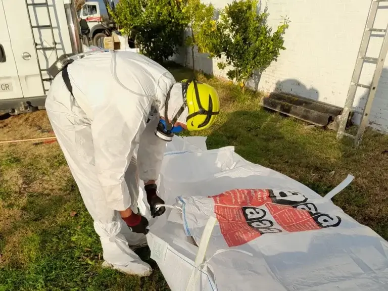Trabajador de retirada de amianto con su ropa EPI envolviendo residuos en una bolsa especial para residuos de amianto