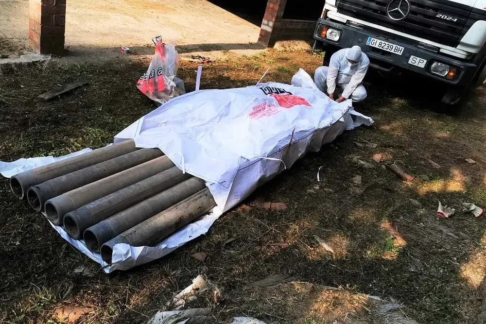 Trabajador de retirada de amianto con su ropa EPI envolviendo residuos en una bolsa especial para residuos de amianto con un camión de la empresa de fondo