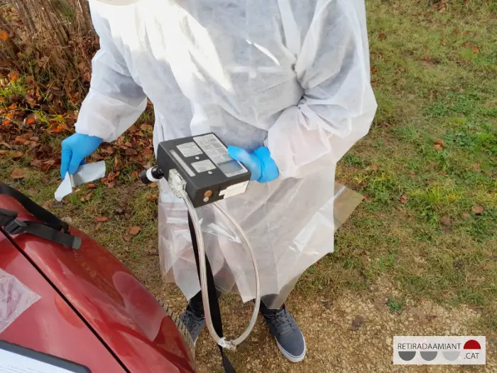 Técnico con guantes y mono de trabajo sobre un vehículo preparando un aparato de medición de fibras de amianto para muestra personal