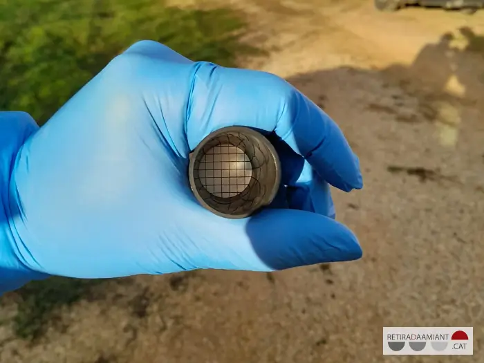 Detall de l'interior d'un filtre d'un aparell que medeix fibres d'amiant en suspensió. El tècnic utilitza guants de làtex