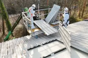 Operarios desmontando placas de uralita de un tejado y colocándolas sobre una grúa