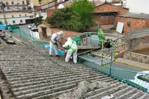 Foto de dos operarios cargando placas de uralita en una grúa durante el desmontaje de un tejado