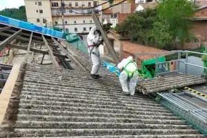 Foto de dos operarios cargando placas de uralita en una grúa durante el desmontaje de un tejado